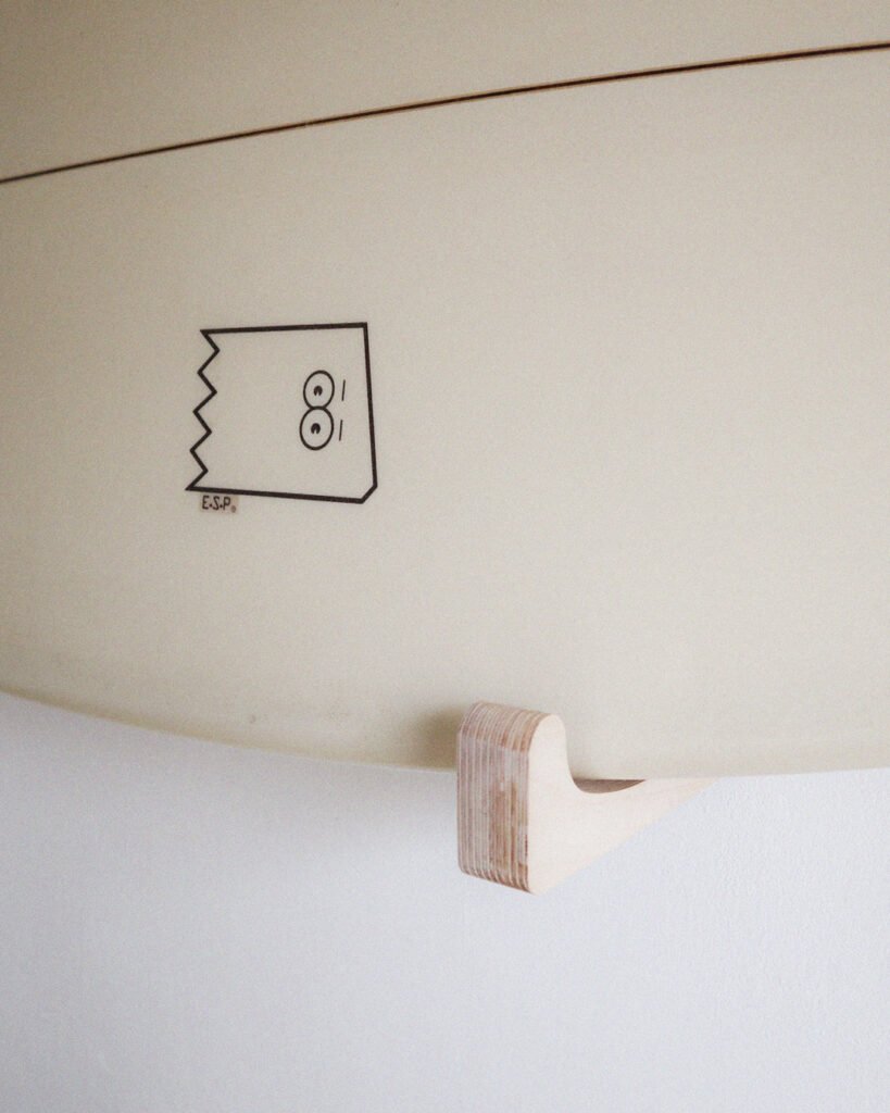 Rack de surf mural horizontal en bois. Un surf est installé dessus.
